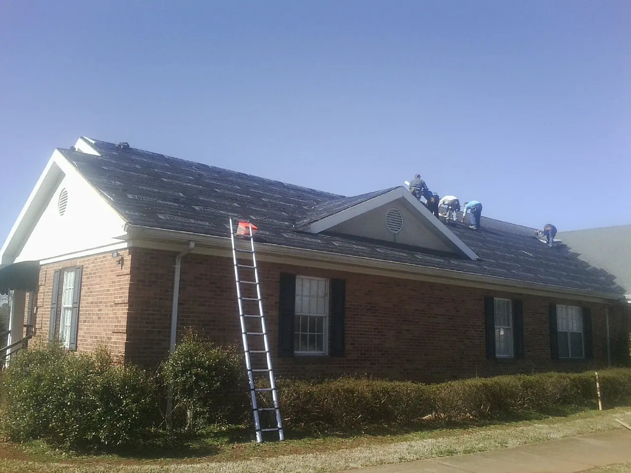 Crew tearing shingles off a brick ranch roof with a ladder set — Metal Roof Repair work by our crew in Cornelius