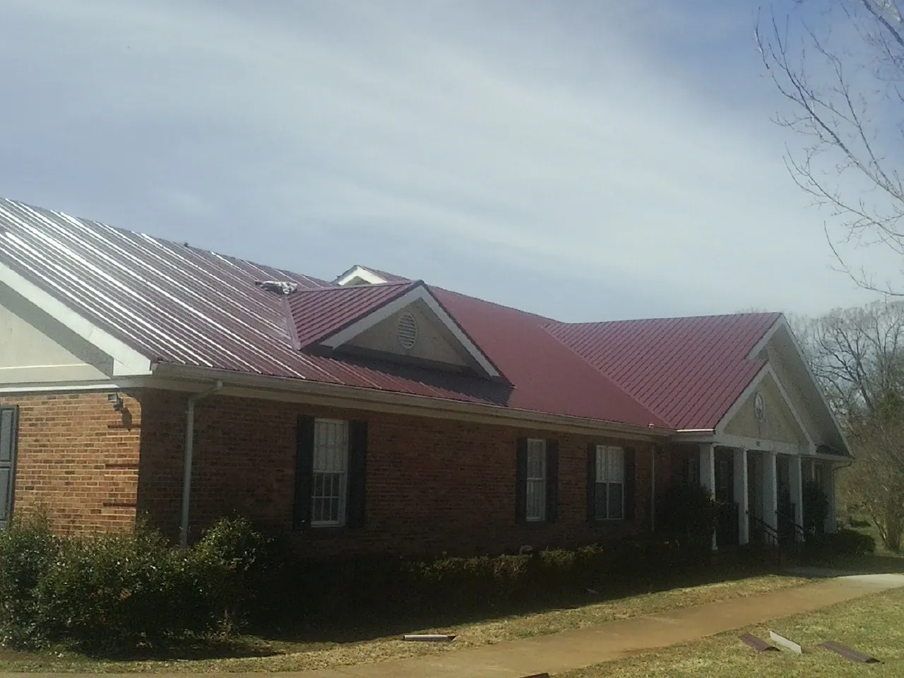 Red metal roof with gabled entries on a long brick building, from a Hail Damage Roof Repair job in Cornelius