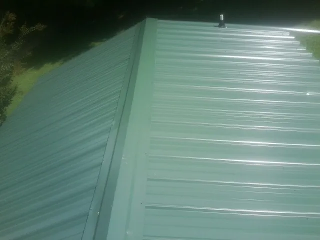 New green metal panels meeting at the ridge of a roof — Flat Roof Repair work by our crew in Cornelius